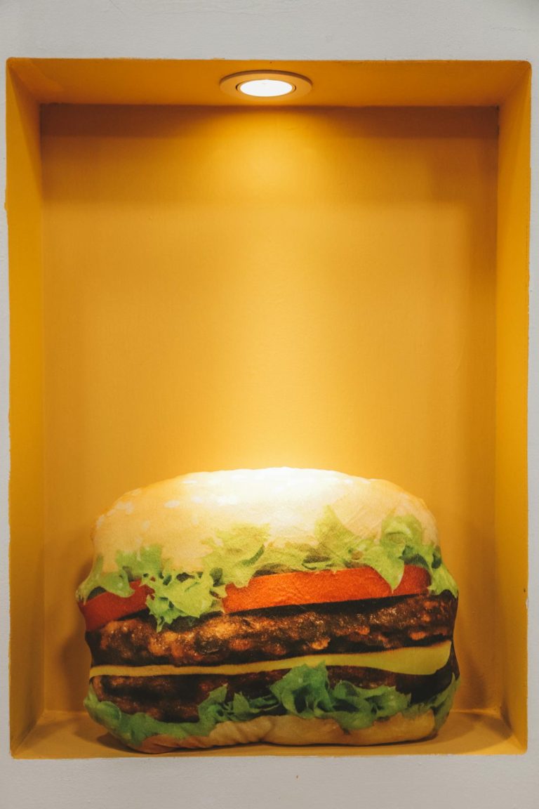 A realistic burger sculpture lit within an indoor wall niche.