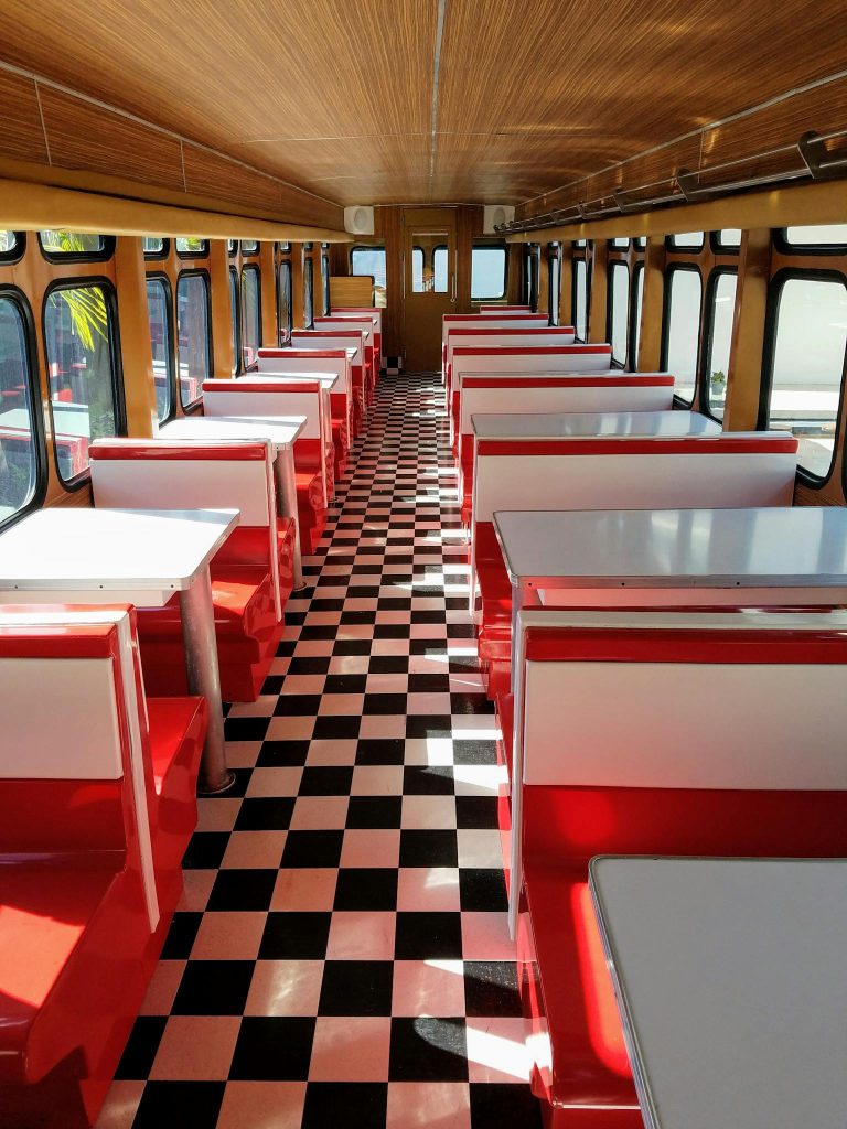 A retro-style diner interior set inside a vintage bus with checkered floors and red booths.